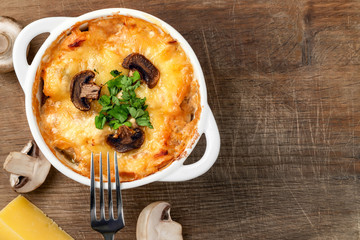 Casserole with chicken, mushrooms and cheese known in Russia as julienne in white bowl with herbs on a wooden board, top view, flat lay, copy space