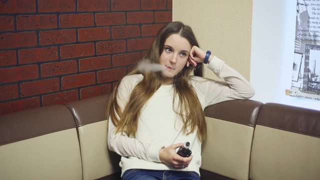 Vaping teenager with problem skin. Young cute caucasian girl smoking an electronic cigarette in the vape bar. Deadly bad habit. Vaping activity. Close up. Social problem.