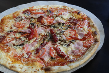 Big tasty and juicy pizza with cheese, bacon, tomatoes, pepper, spices on paper parchment close-up in a cafe. View from above. Italian pizza. Fast food concept. Free space for your text.