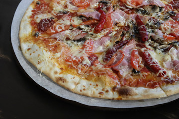 Big tasty and juicy pizza with cheese, bacon, tomatoes, pepper, spices on paper parchment close-up in a cafe. View from above. Italian pizza. Fast food concept. Free space for your text.