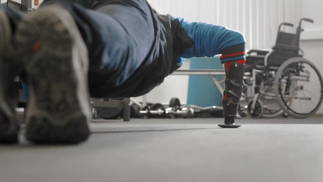 The athlete with a prosthetic arm is pushing out. Does exercise on the floor while lying. Professional prosthetic arm for sports.
