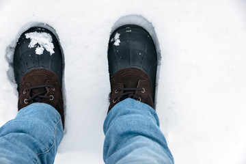 Person standing in the snow wearing blue jeans with snow covered boots.