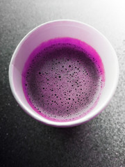 Cup of black currant smothie in cafeteria. Top view macro photo of organic drink with bubbles of foam. Сardboard round object on gray background.