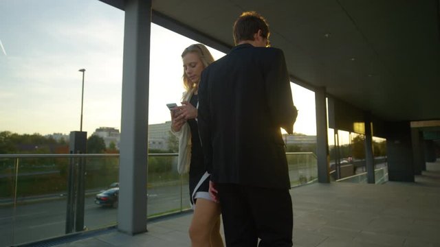 CLOSE UP, LENS FLARE, SLOW MOTION: Courteous business professionals apologize after bumping into each other as they walk and text to work at sunrise. Businesswoman and man collide on the sunlit street