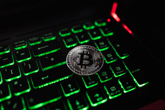 Bitcoin silver coin lie on the notebook lighted keyboard. 