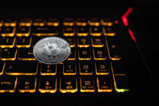 Bitcoin silver coin lie on the notebook lighted keyboard. 