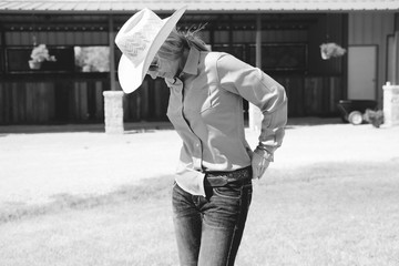 Woman tucking in button up shirt, black and white image of western industry cowgirl wearing cowboy hat.