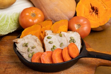 Sliced pork meat baked in the oven with pumpkin, carrots and pumpkin seeds, served in a small cast iron pan among seasonal vegetables.