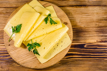 Sliced cheese and parsley on a wooden cutting board. Top view