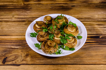 Plate with baked champignons, dill and parsley on a wooden table