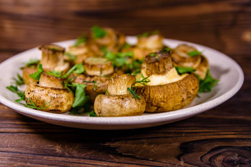 Plate with baked champignons, dill and parsley on a wooden table