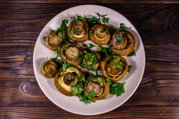 Plate with baked champignons, dill and parsley on a wooden table. Top view