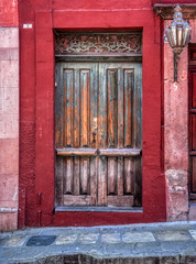 A beautiful very old faded wooden door with a red cement frame and a beautiful vintage lamp