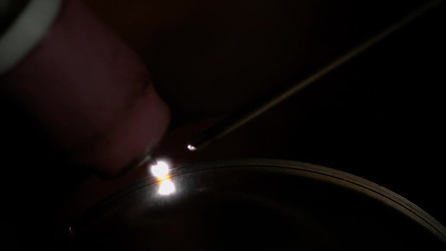 SLOW MOTION, MACRO, DOF: Unrecognizable experienced metalworker welds two pieces of titanium together while crafting a car muffler. Welder tacking a piece of metal while crafting an exhaust pipe.