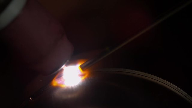 SLOW MOTION, MACRO, DOF: Flames coming out of an industrial welding machine create a weld on an automobile exhaust pipe. Metalworker welds two pieces of titanium together while crafting a car muffler.