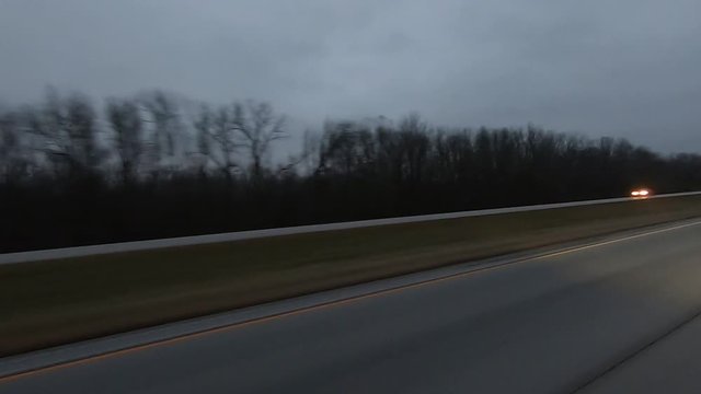 Drivers POV out of the side window while driving red vehicle down an interstate at dusk on a rainy, cloudy day;  point of view