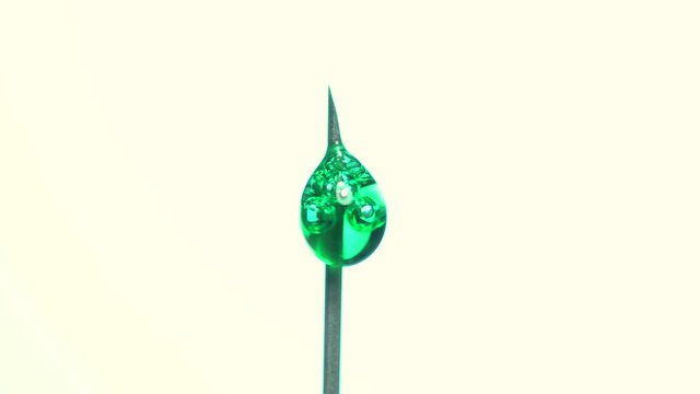 Micro bubbles forming from green liquid dripping out from hypodermic needle extreme maco on white background