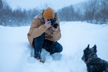 A man photographs his dog on winter walk in the snow