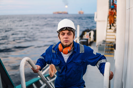 Marine Deck Officer or Chief mate seaman on deck of offshore vessel or ship , wearing PPE personal protective equipment - helmet, coverall. he climbs the ladder