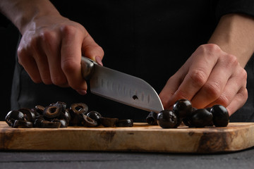 The cook on a wooden board cuts black olives closeup, macro