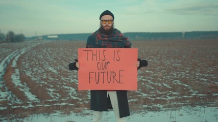 Young bearded man activist with ecology poster This is our Future in field environment nature earth pollution world protection trash volunteer mask waste recycle garbage ecological slow motion