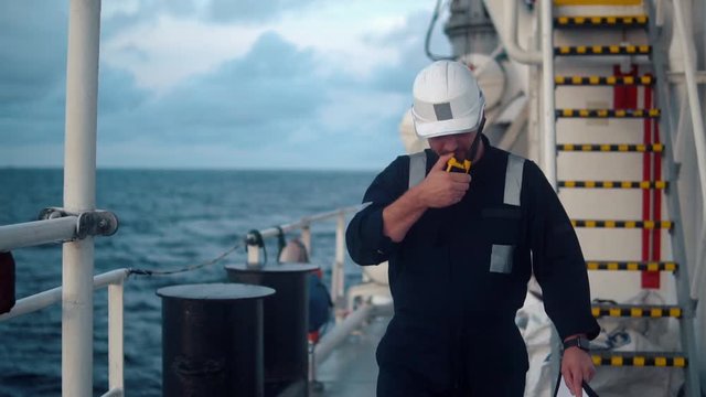 Marine Deck Officer or Chief mate on deck of vessel or ship . He holds VHF walkie-talkie radio in hands. Ship communication