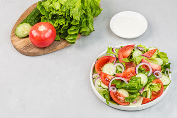 Healthy vegetarian dish on table, vegetable salad with fresh tomato, cucumber, lettuce, red onion on gray concrete background. Diet menu. mockup, template