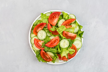 Healthy vegetarian dish on table, vegetable salad with fresh tomato, cucumber, lettuce, red onion on gray concrete background. Diet menu. Top view. Flat lay, mockup, template with copy space