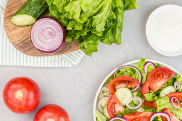 Healthy vegetarian dish on table, vegetable salad with fresh tomato, cucumber, lettuce, red onion on gray concrete background. Diet menu. Top view. Flat lay, mockup, template