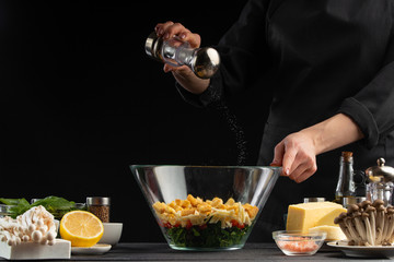 A professional cook prepares a fresh salad with spinach leaves, sprinkled with salt and fresh ingredients, Freezing in motion. Vegetarian and healthy food. Organic food. On a black background.