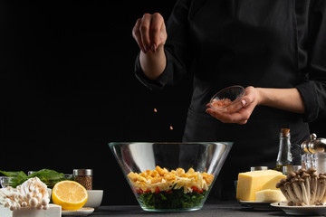 A professional chef cooks a fresh and healthy salad by sowing coarse salt, Freezing in motion. Organic and wholesome food. Healthy nutrition and vitamins. Advertising photo, on black background.