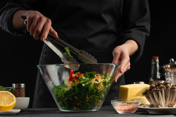 Cooking a salad, the cook prepares a salad on a dark background with ingredients. Delicious and healthy food.