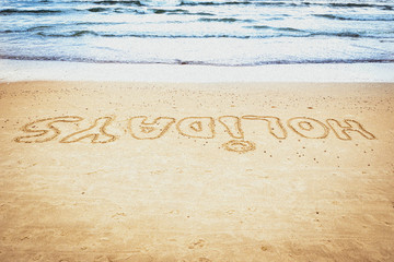Odręczny napis holidays - wakacje  na piasku nad morzem