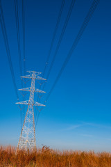 Electric pole and electric cable on the field in the countryside with blue sky.