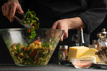 A professional cook prepares a fresh salad with spinach leaves, mixes the salad on the background with fresh ingredients, Freezing in motion. Vegetarian and healthy food. Organic food