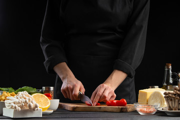 The chef cuts cherry tomatoes to prepare a tasty and fresh salad. Vegetarian and fresh food, gastronomy and cooking, recipe book and recipes. On a black background