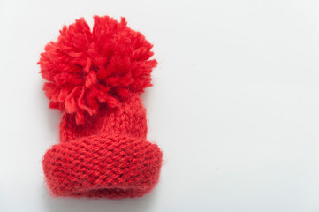 Red knitted wool beanie hat on white table top view.