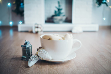 Festive interior: coffee Cup with foam and marshmallows inside next to glass cones and decorative candles on the background of the fireplace, Christmas tree and boce. The concept of New year, healthy 