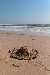 A sand castle surrounded by rocks is bounded by children at a beautiful beach.