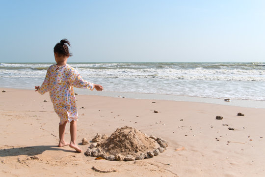 An Asian Girl Is Building A Sand Castle With Sand And Rocks At A Beautiful Beach In A Clear Day.