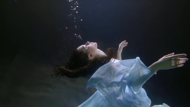 magic fairy is floating underwater in depth of swimming pool in darkness