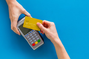 Contactless payment, paypass. Hand hold bank card near terminal on blue background top-down copy...