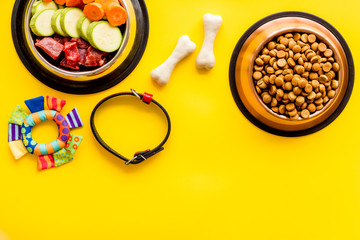 Pet care concept. Dry feed and meat in bowls near collar and bones on yellow background top view copy space
