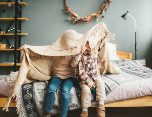 Two happy sibling children hiding under plaid