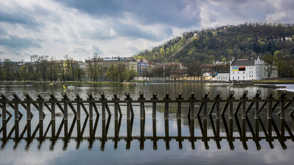 Wooden barrier in moldava river in Prague. East part of the city viewed from the other side of the river