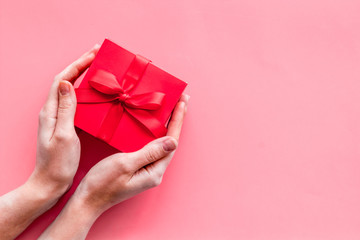 Give a gift on Valentine's Day. Women hand hold beautiful red present box on pink background top-down copy space