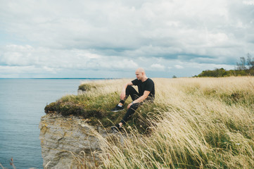 Naklejka na ściany i meble A tourist spending time on grass on the edge of the rocky coast of the Baltic sea