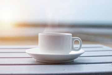 A cup of white coffee is on the white wooden table by the sea