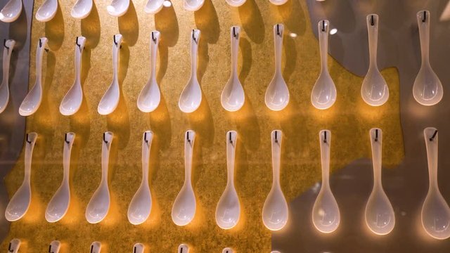 Japanese ramen spoons on wall in rows, moving gimbal stabilized shot in 4k, white soup spoons on a gold and silver background