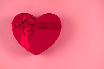 Red gift box heart shape with red ribbon on a pastel pink background, gift concept Valentine day, top wiev, copy space